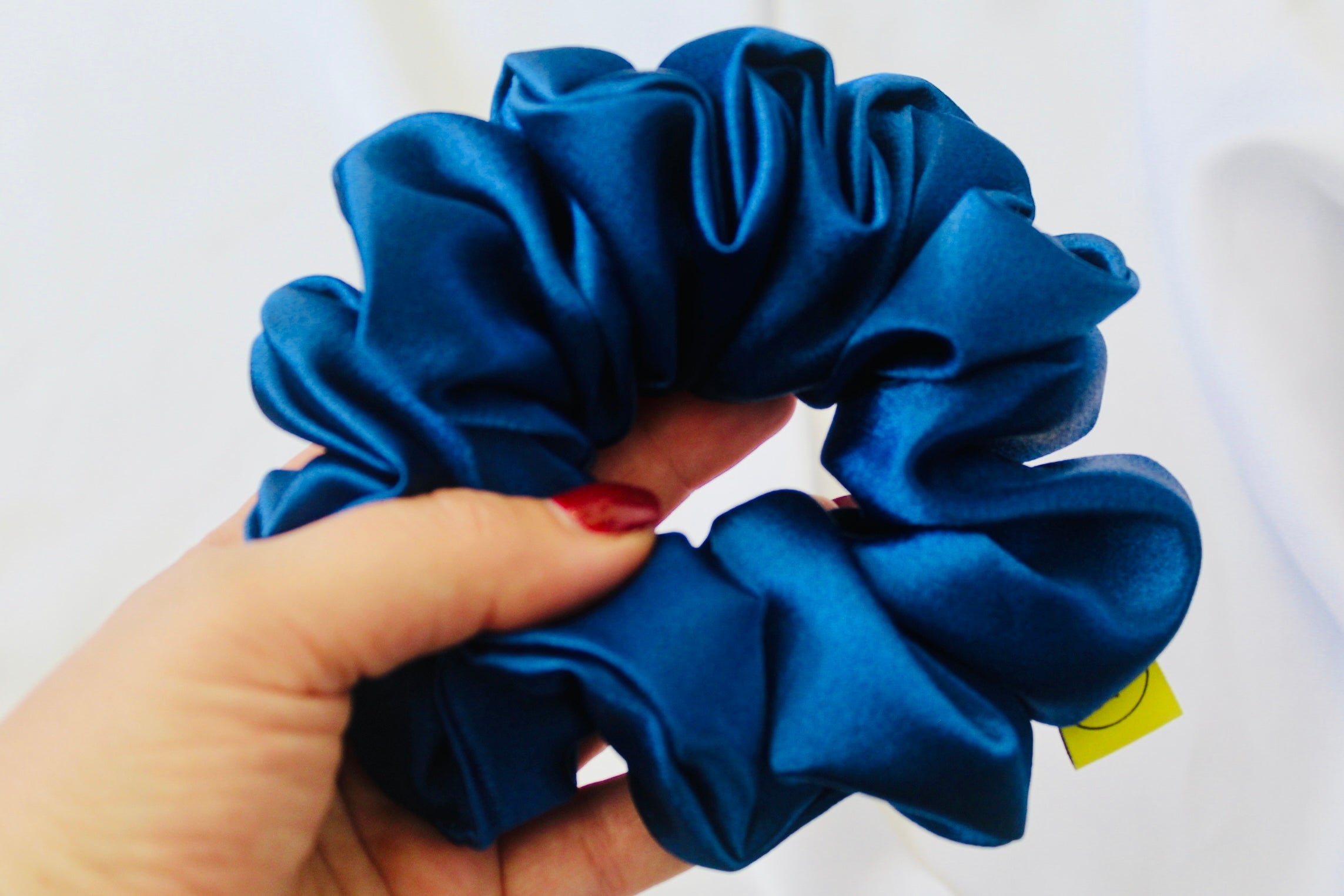 A satin scrunchie in a striking royal blue shade with a silky glossy texture and a ruched design. Crafted from satin this scrunchie feels smooth and cool to the touch. The bold royal blue colour stands out beautifully, making it a statement piece for both casual and evening looks. The gathered satin fabric creates a full textured effect over the elastic ensuring a secure hold.