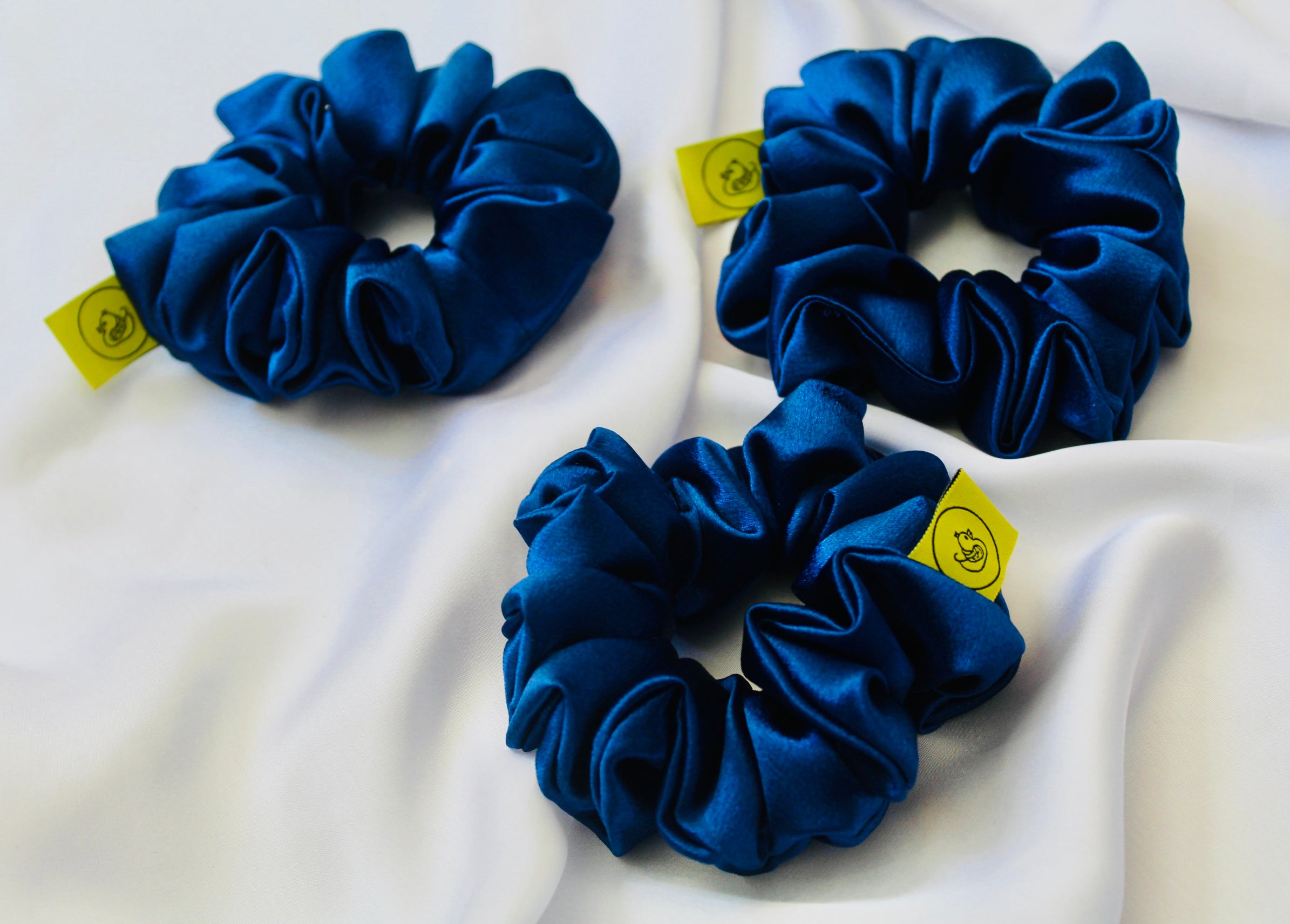 A satin scrunchie in a striking royal blue shade with a silky glossy texture and a ruched design. Crafted from satin this scrunchie feels smooth and cool to the touch. The bold royal blue colour stands out beautifully, making it a statement piece for both casual and evening looks. The gathered satin fabric creates a full textured effect over the elastic ensuring a secure hold.