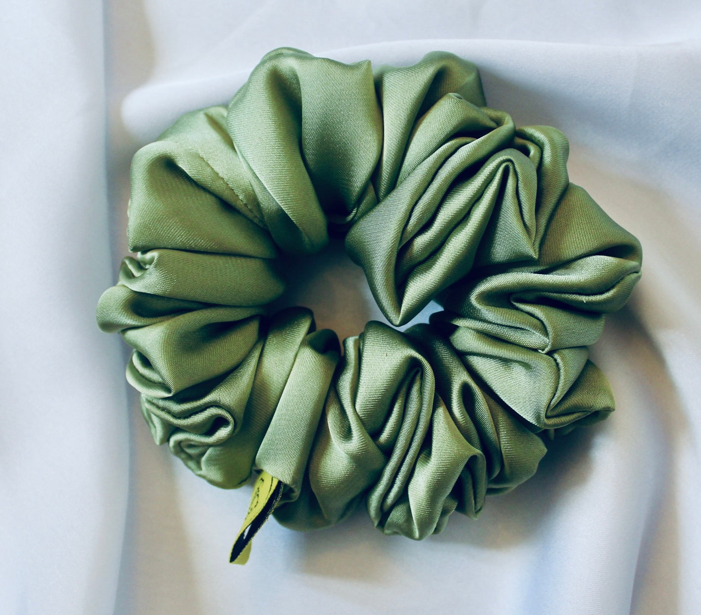 A satin scrunchie in a light green shade with a silky, glossy finish and a ruched design.  Crafted from smooth satin, this scrunchie feels soft and sleek against the hair.  The green tone has a timeless, earthy quality, perfect for both everyday wear and festive styling.  Its ruched fabric is stretched over an elastic band, providing a secure yet comfortable fit.