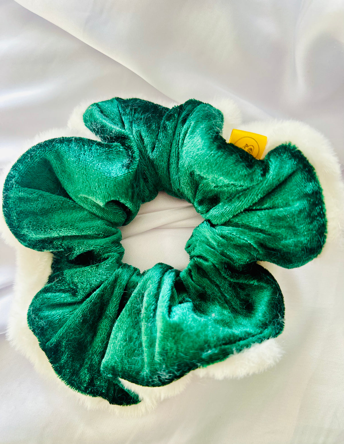 A green velvet Christmas scrunchie with white faux fur trim on a white surface.
