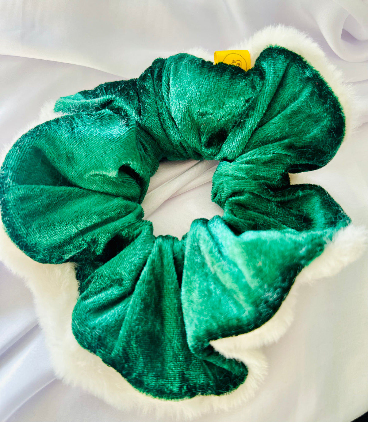 A green velvet Christmas scrunchie with white faux fur trim on a white surface.