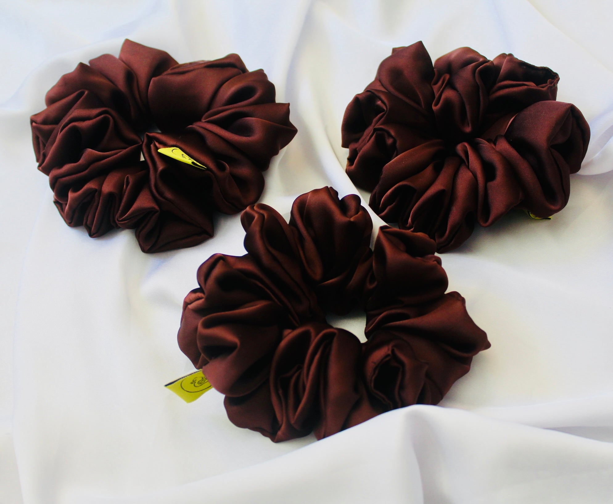 A satin scrunchie in a rich chocolate brown shade with a smooth and shiny texture and a ruched design.  This scrunchie is made from glossy satin giving it a soft, luxurious touch.  The deep chocolate brown colour is both bold and neutral, making it easy to style with a wide range of outfits.  The fabric is softly ruched over elastic, creating volume while remaining comfortable to wear.