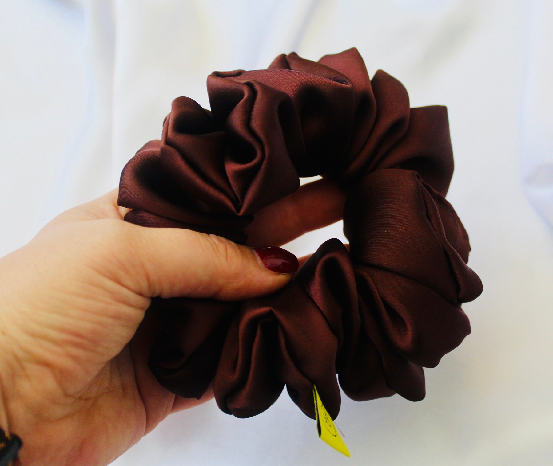 A satin scrunchie in a rich chocolate brown shade with a smooth and shiny texture and a ruched design.  This scrunchie is made from glossy satin giving it a soft, luxurious touch.  The deep chocolate brown colour is both bold and neutral, making it easy to style with a wide range of outfits.  The fabric is softly ruched over elastic, creating volume while remaining comfortable to wear.