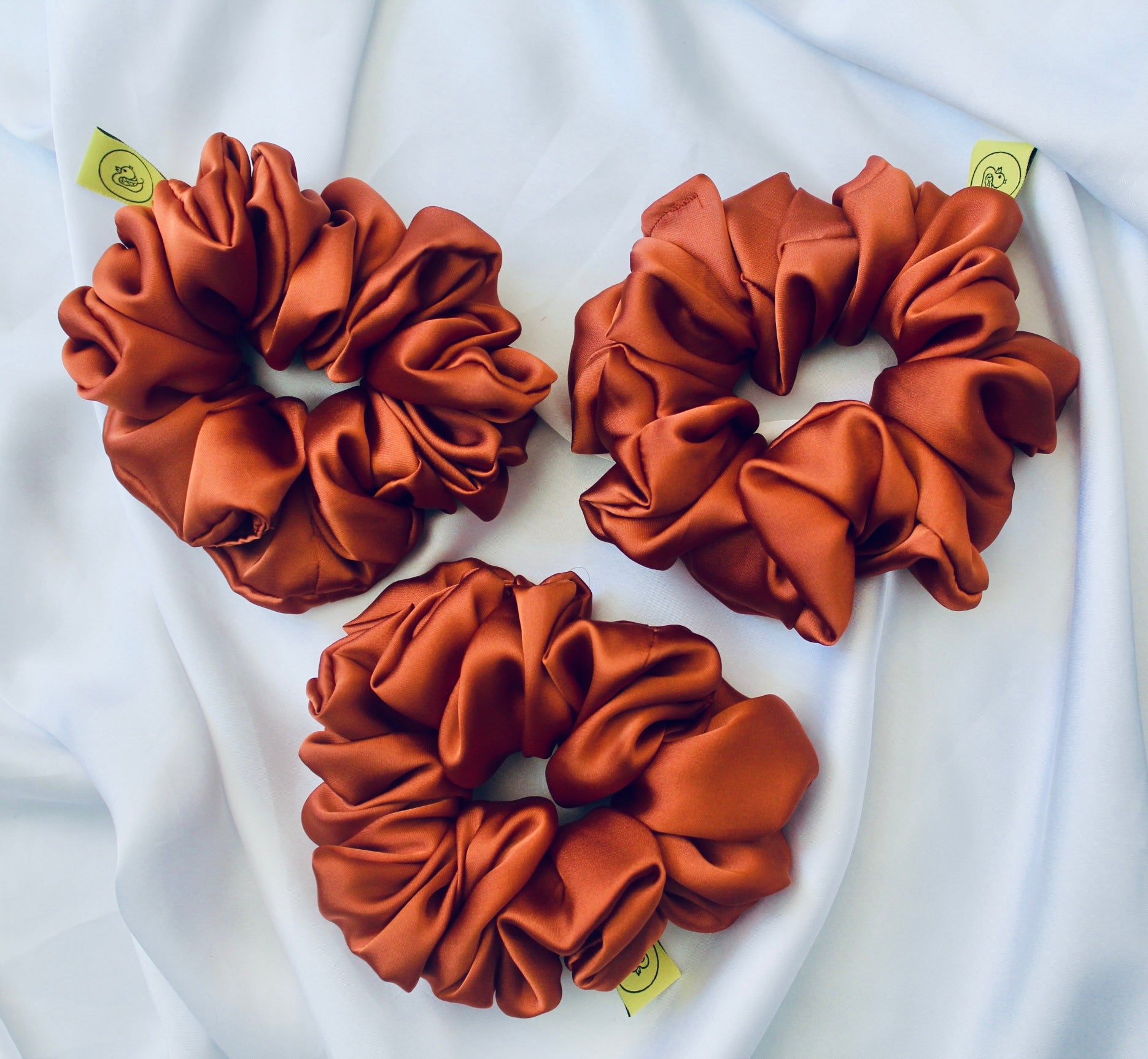 A satin scrunchie in a warm burnt orange shade with a smooth glossy texture and a ruched design.  This scrunchie is made from satin giving it a silky and lightweight feel.  The rich burnt orange colour captures the warmth of autumn leaves, making it perfect seasonal accessory.  The gathered fabric sits on an elastic core, creating a full ruffled look while keeping your hairstyle secure and comfortable.