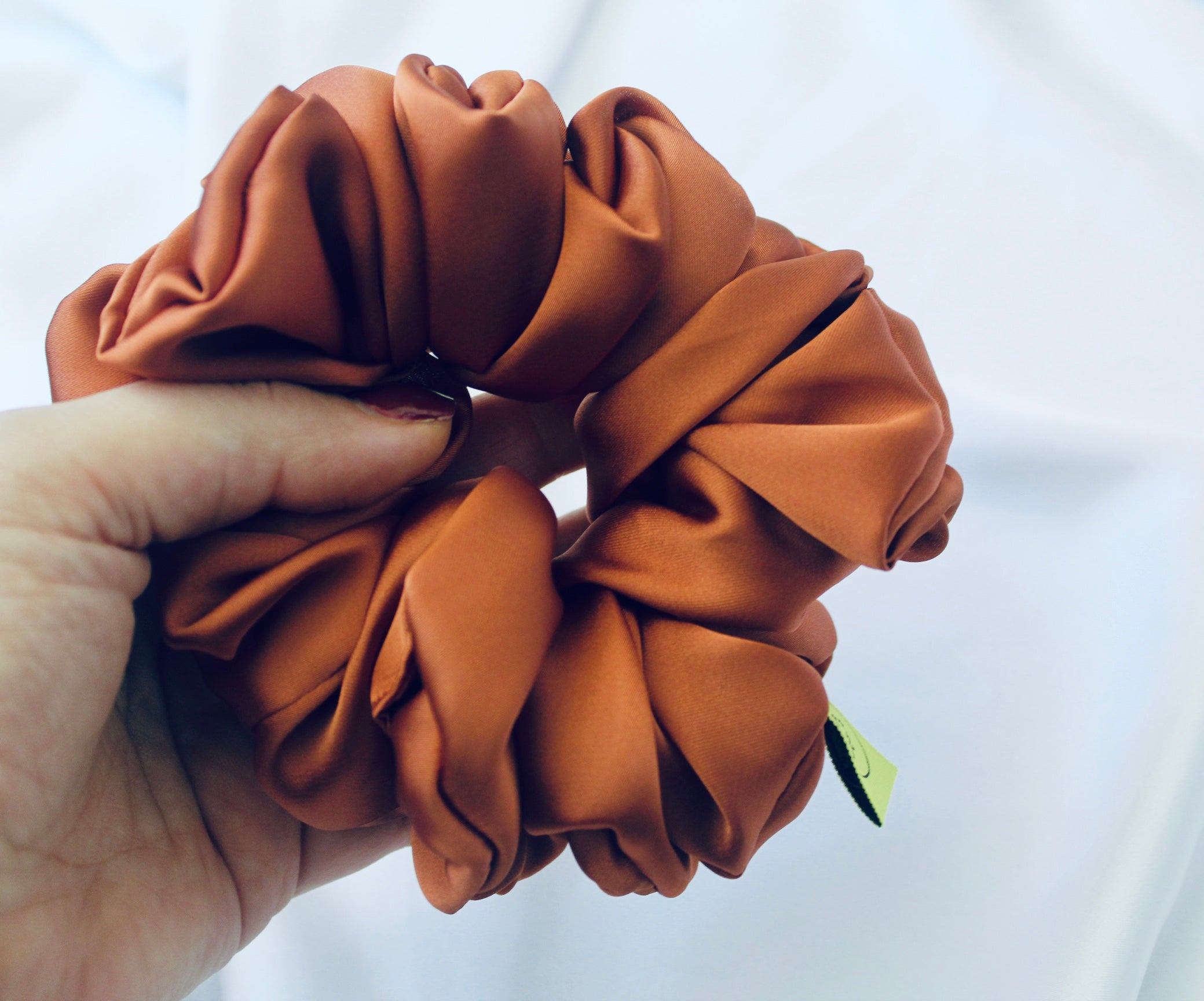 A satin scrunchie in a warm burnt orange shade with a smooth glossy texture and a ruched design.  This scrunchie is made from satin giving it a silky and lightweight feel.  The rich burnt orange colour captures the warmth of autumn leaves, making it perfect seasonal accessory.  The gathered fabric sits on an elastic core, creating a full ruffled look while keeping your hairstyle secure and comfortable.