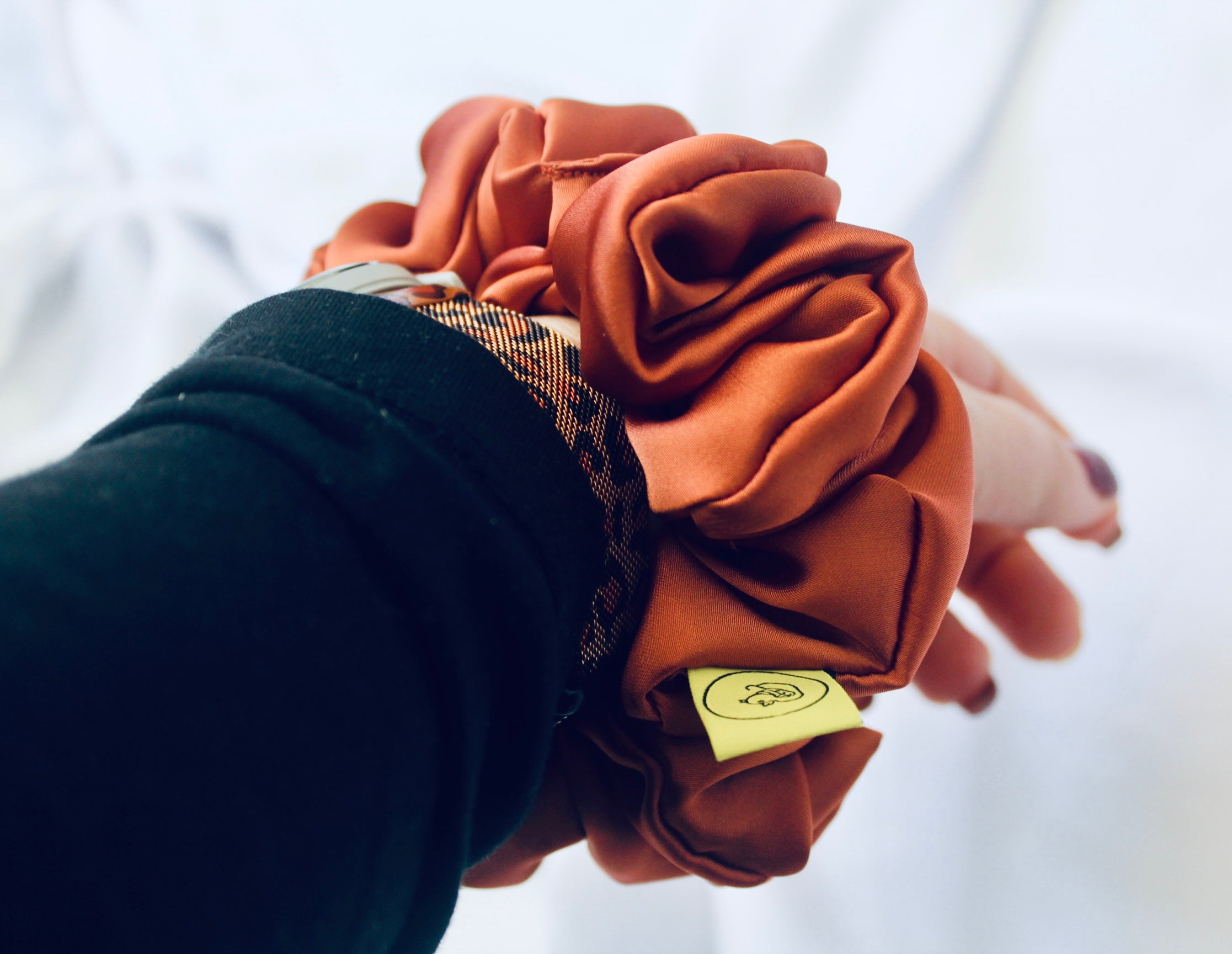 A satin scrunchie in a warm burnt orange shade with a smooth glossy texture and a ruched design.  This scrunchie is made from satin giving it a silky and lightweight feel.  The rich burnt orange colour captures the warmth of autumn leaves, making it perfect seasonal accessory.  The gathered fabric sits on an elastic core, creating a full ruffled look while keeping your hairstyle secure and comfortable.