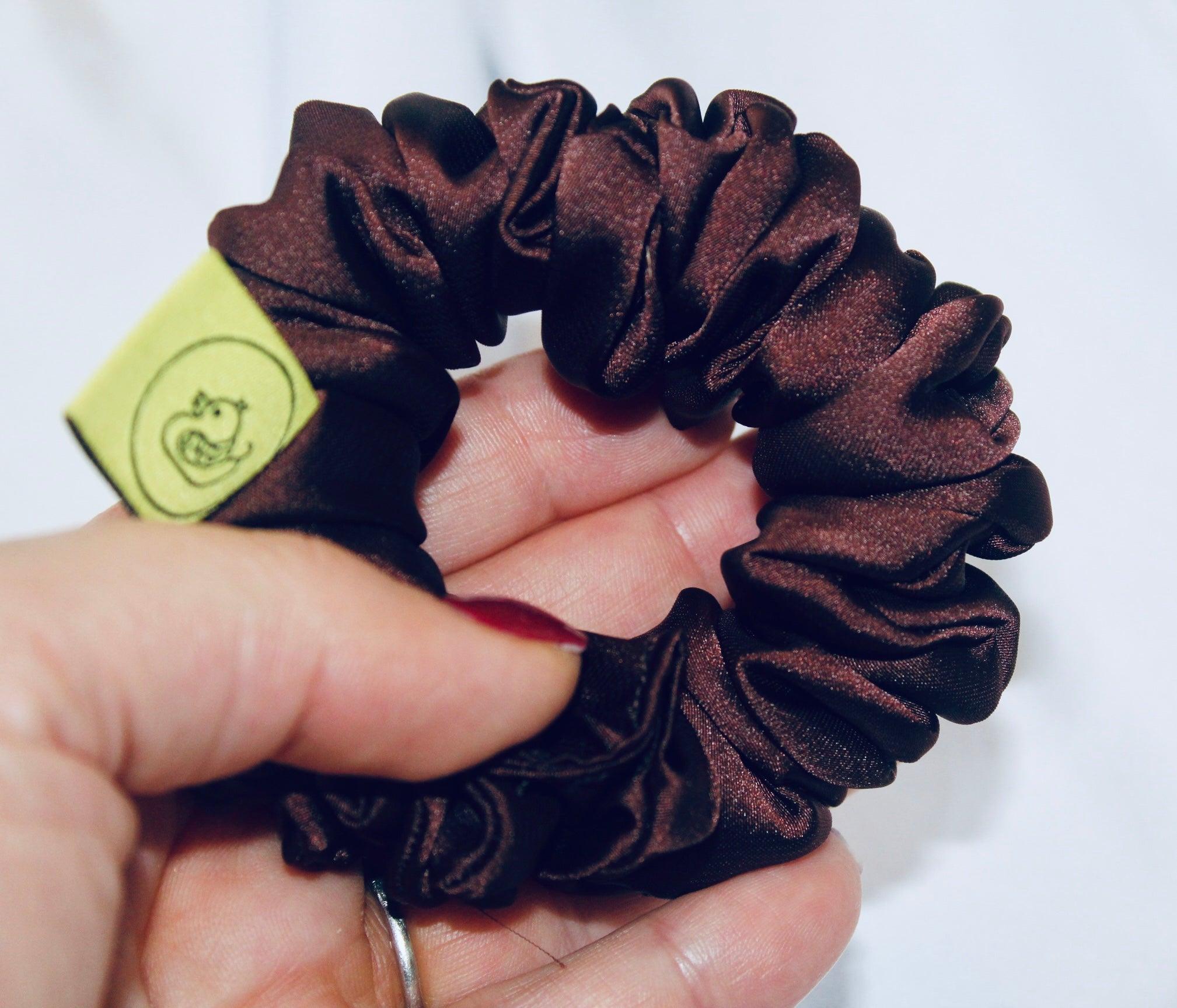 A satin scrunchie in a rich chocolate brown shade with a smooth and shiny texture and a ruched design.  This scrunchie is made from glossy satin giving it a soft, luxurious touch.  The deep chocolate brown colour is both bold and neutral, making it easy to style with a wide range of outfits.  The fabric is softly ruched over elastic, creating volume while remaining comfortable to wear.
