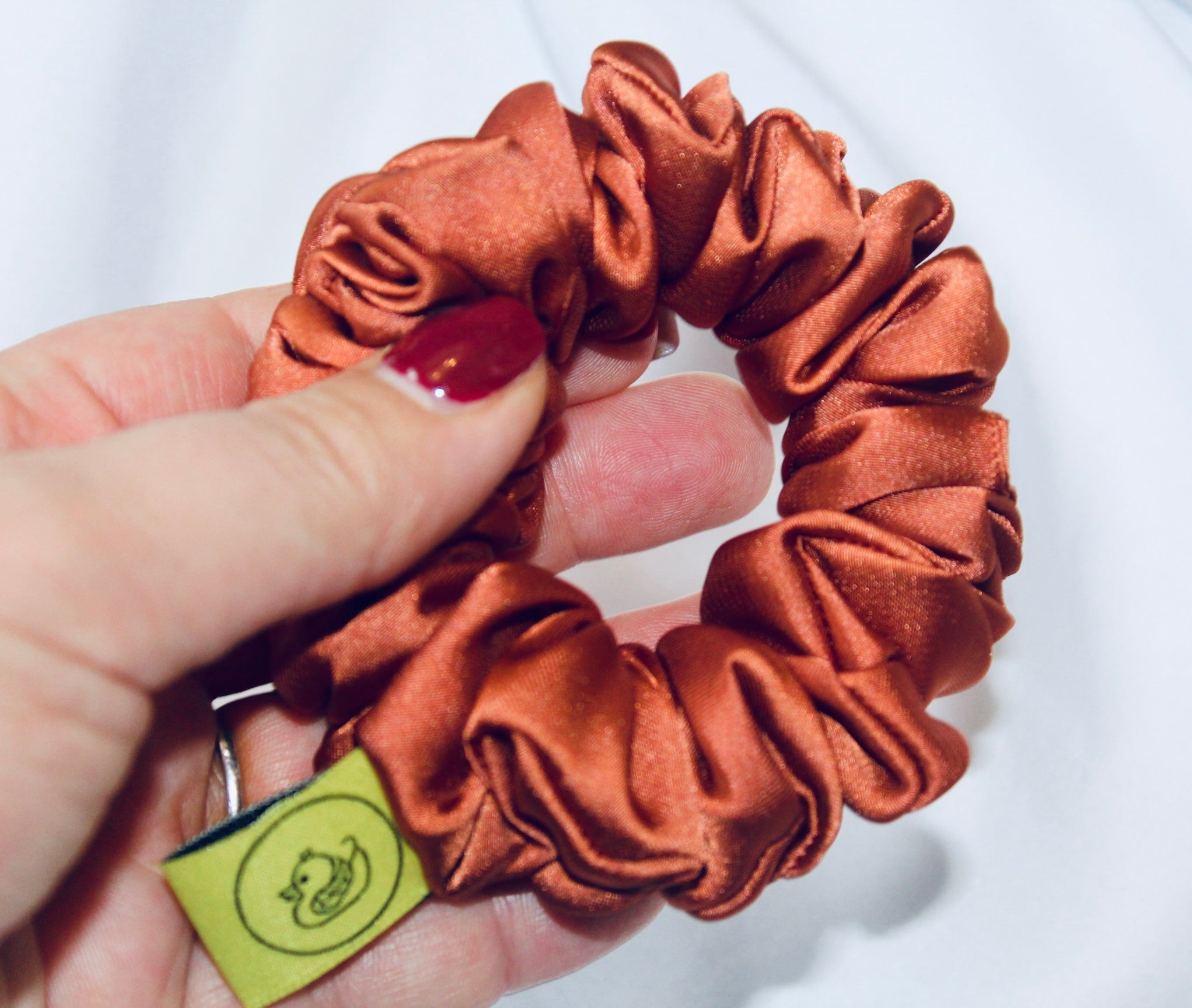 A satin scrunchie in a warm burnt orange shade with a smooth glossy texture and a ruched design.  This scrunchie is made from satin giving it a silky and lightweight feel.  The rich burnt orange colour captures the warmth of autumn leaves, making it perfect seasonal accessory.  The gathered fabric sits on an elastic core, creating a full ruffled look while keeping your hairstyle secure and comfortable.