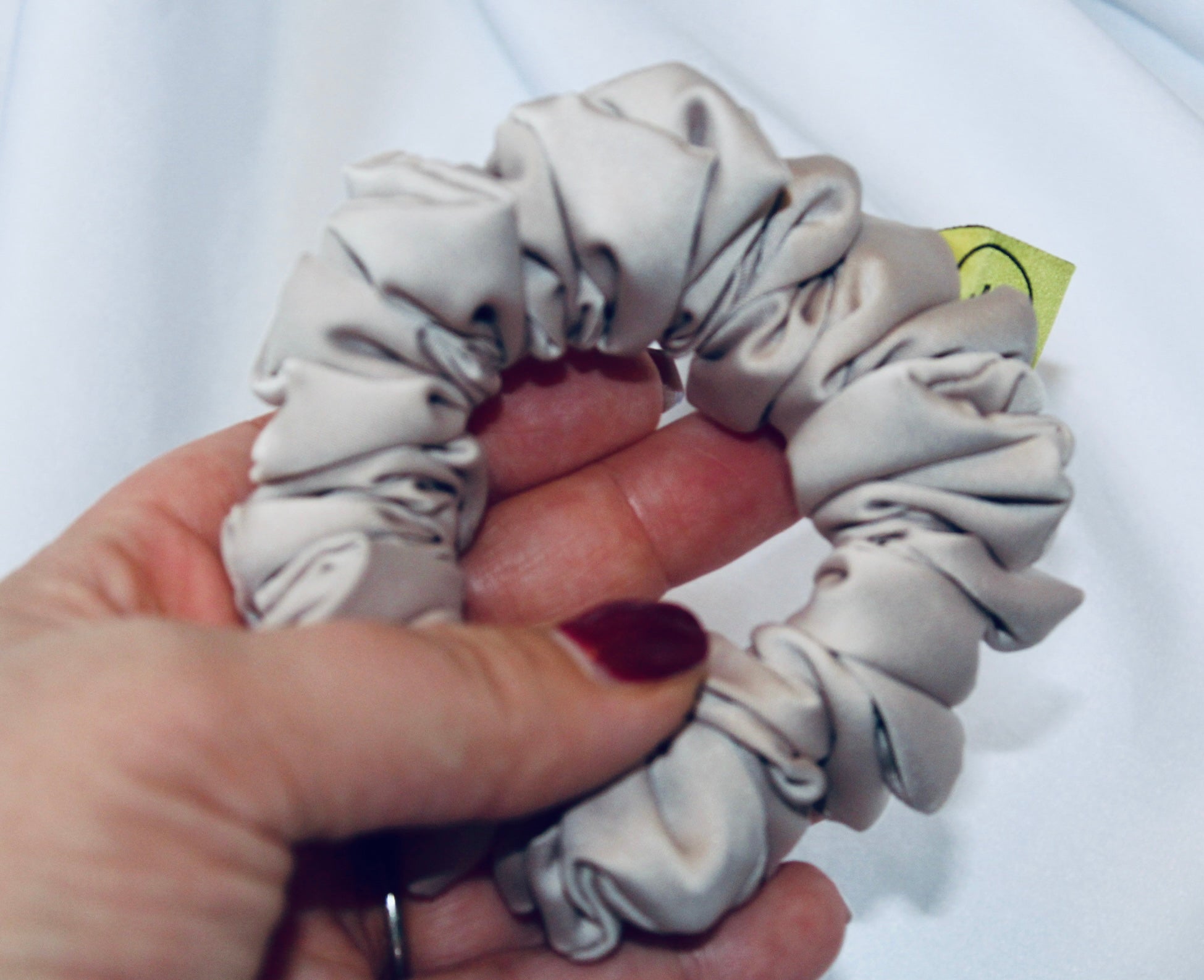 A satin hair scrunchie in a soft taupe beigge with a smooth glossy texture and a ruched design.  This scrunchie is made from satin, giving it a silky, luxurious feel.  The soft taupe shade is a neutral tone that pairs well with any outfit, making it a timeless everyday essential.  It's fabric is gathered along an elastic core, creating a full, ruffled look while staying secure and comfortable in the hair.