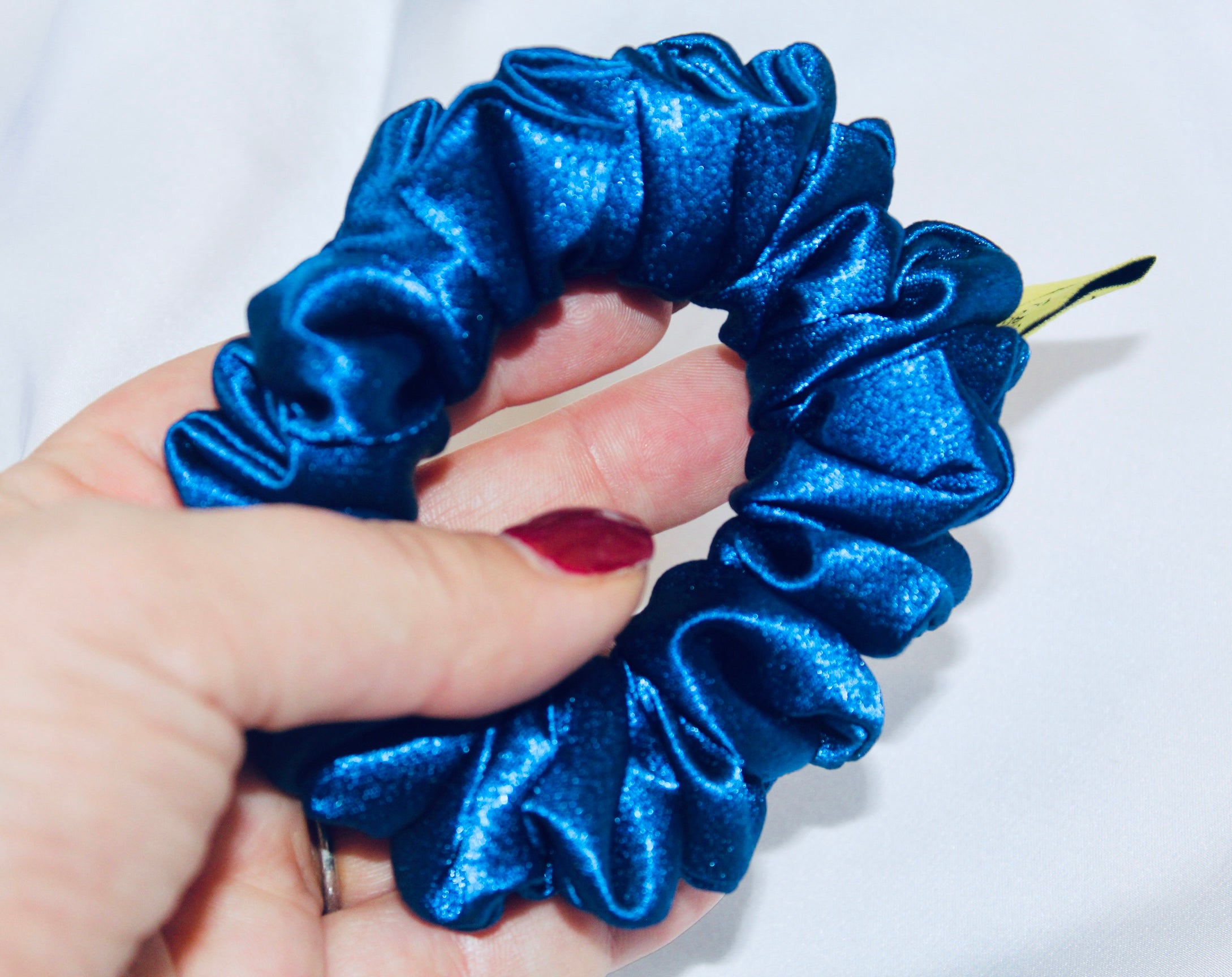 A satin scrunchie in a striking royal blue shade with a silky glossy texture and a ruched design.  Crafted from satin this scrunchie feels smooth and cool to the touch.  The bold royal blue colour stands out beautifully, making it a statement piece for both casual and evening looks.  The gathered satin fabric creates a full textured effect over the elastic ensuring a secure hold.