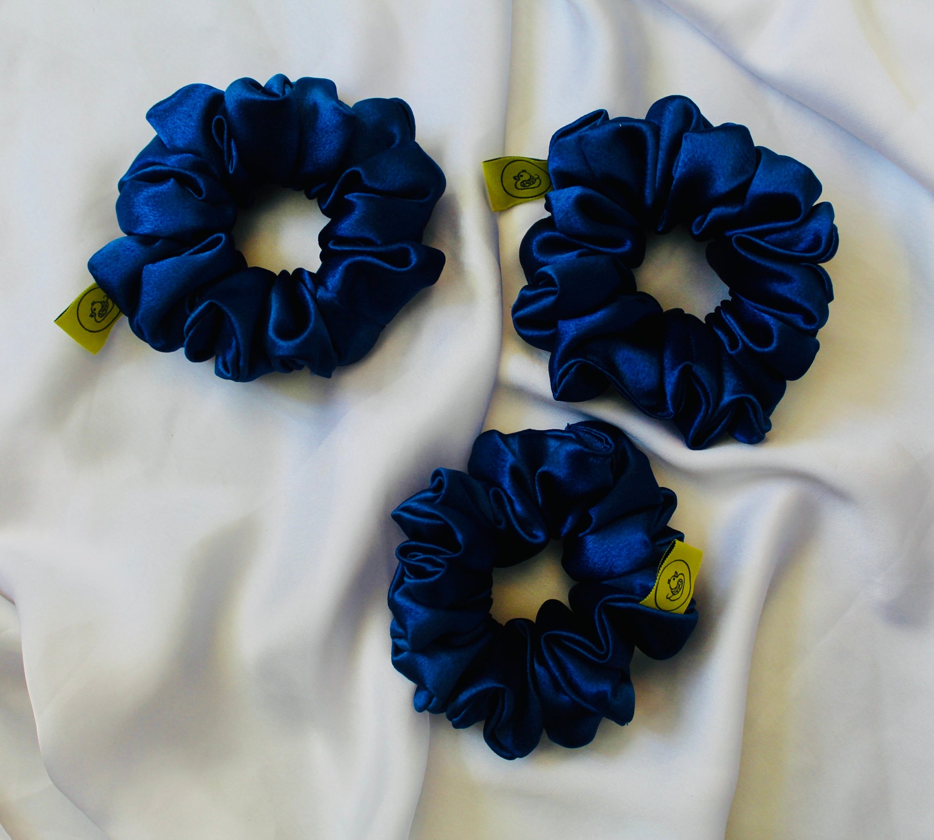 A satin scrunchie in a striking royal blue shade with a silky glossy texture and a ruched design.  Crafted from satin this scrunchie feels smooth and cool to the touch.  The bold royal blue colour stands out beautifully, making it a statement piece for both casual and evening looks.  The gathered satin fabric creates a full textured effect over the elastic ensuring a secure hold.