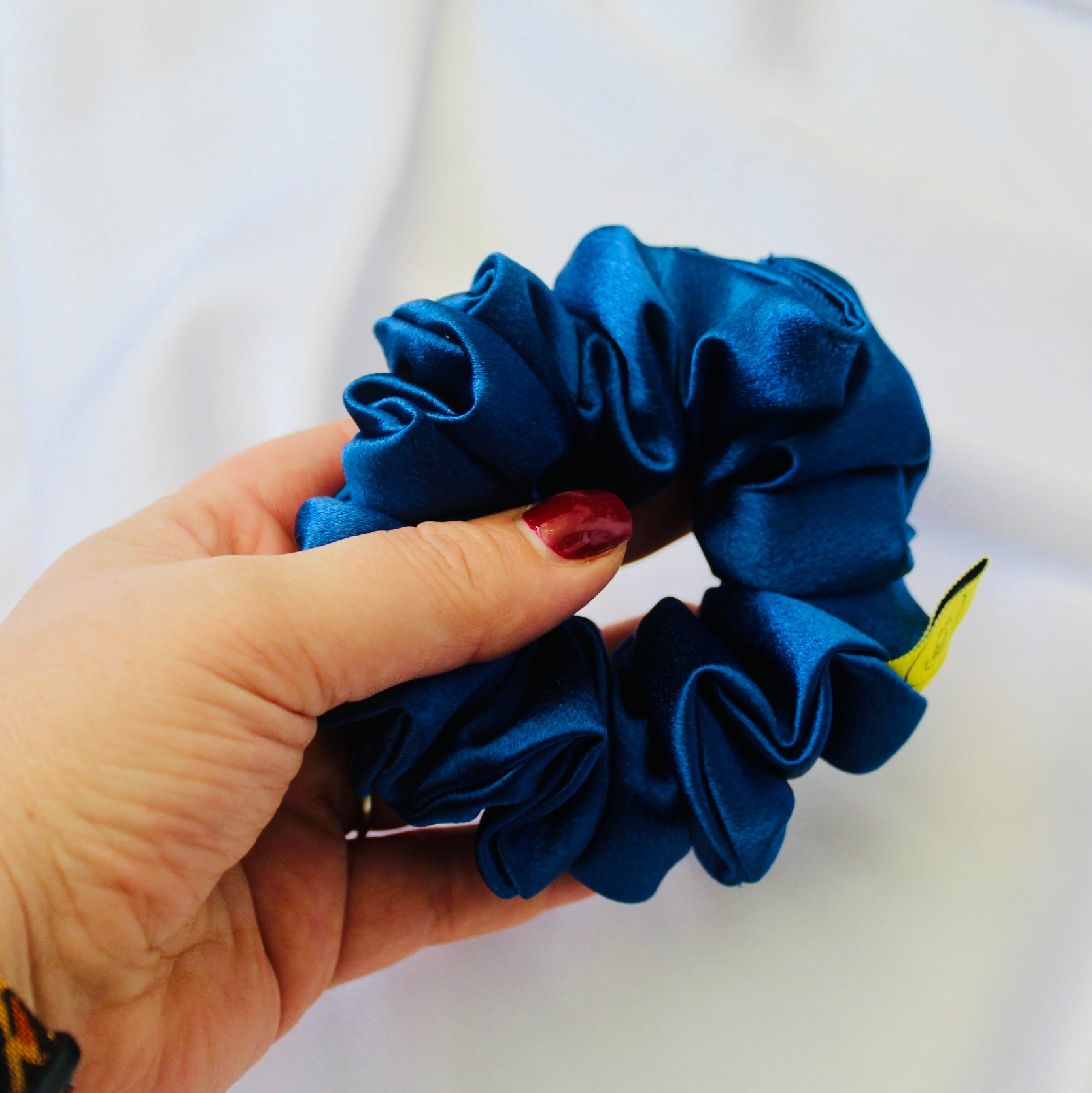 A satin scrunchie in a striking royal blue shade with a silky glossy texture and a ruched design.  Crafted from satin this scrunchie feels smooth and cool to the touch.  The bold royal blue colour stands out beautifully, making it a statement piece for both casual and evening looks.  The gathered satin fabric creates a full textured effect over the elastic ensuring a secure hold.