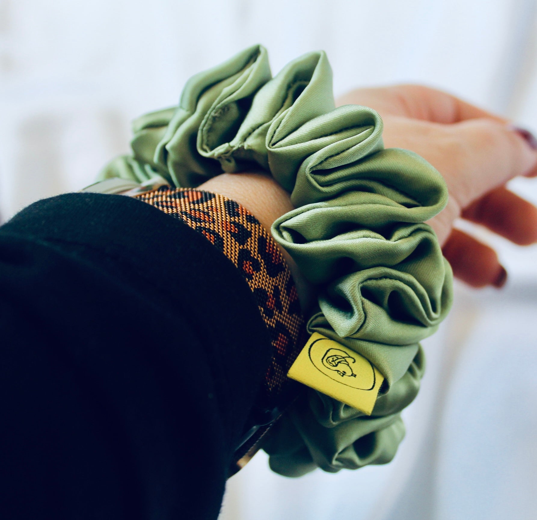 A satin scrunchie in a light green shade with a silky, glossy finish and a ruched design.  Crafted from smooth satin, this scrunchie feels soft and sleek against the hair.  The green tone has a timeless, earthy quality, perfect for both everyday wear and festive styling.  Its ruched fabric is stretched over an elastic band, providing a secure yet comfortable fit.