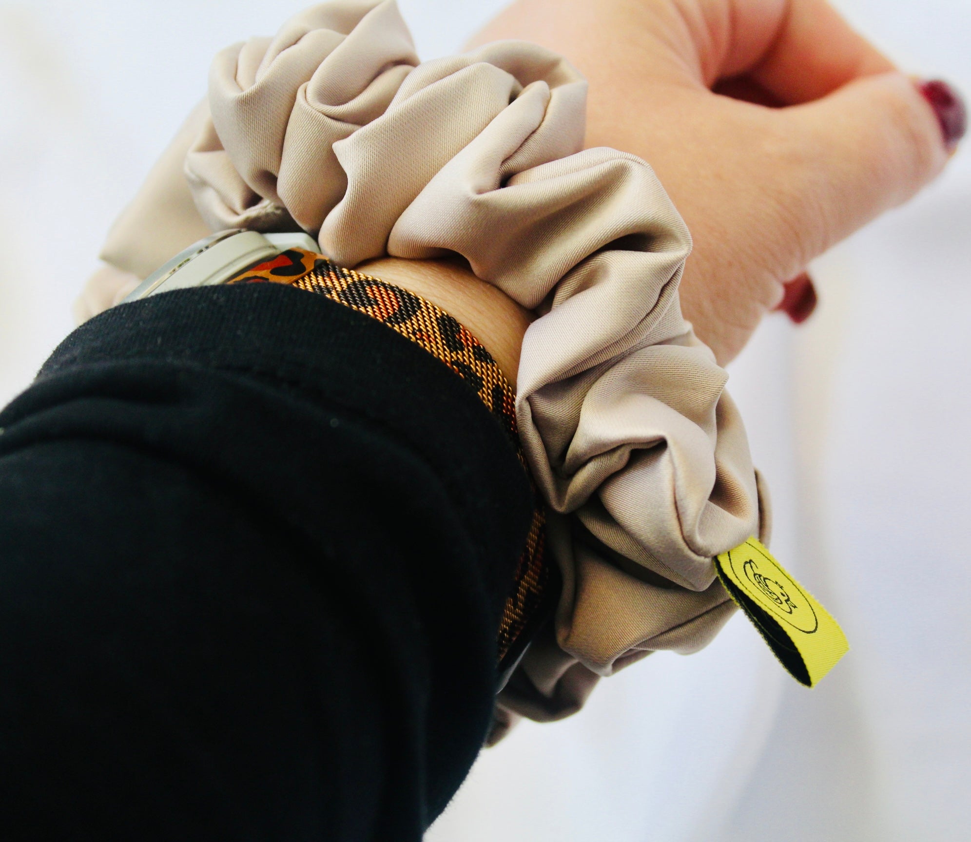 A satin hair scrunchie in a soft taupe beigge with a smooth glossy texture and a ruched design.  This scrunchie is made from satin, giving it a silky, luxurious feel.  The soft taupe shade is a neutral tone that pairs well with any outfit, making it a timeless everyday essential.  It's fabric is gathered along an elastic core, creating a full, ruffled look while staying secure and comfortable in the hair.
