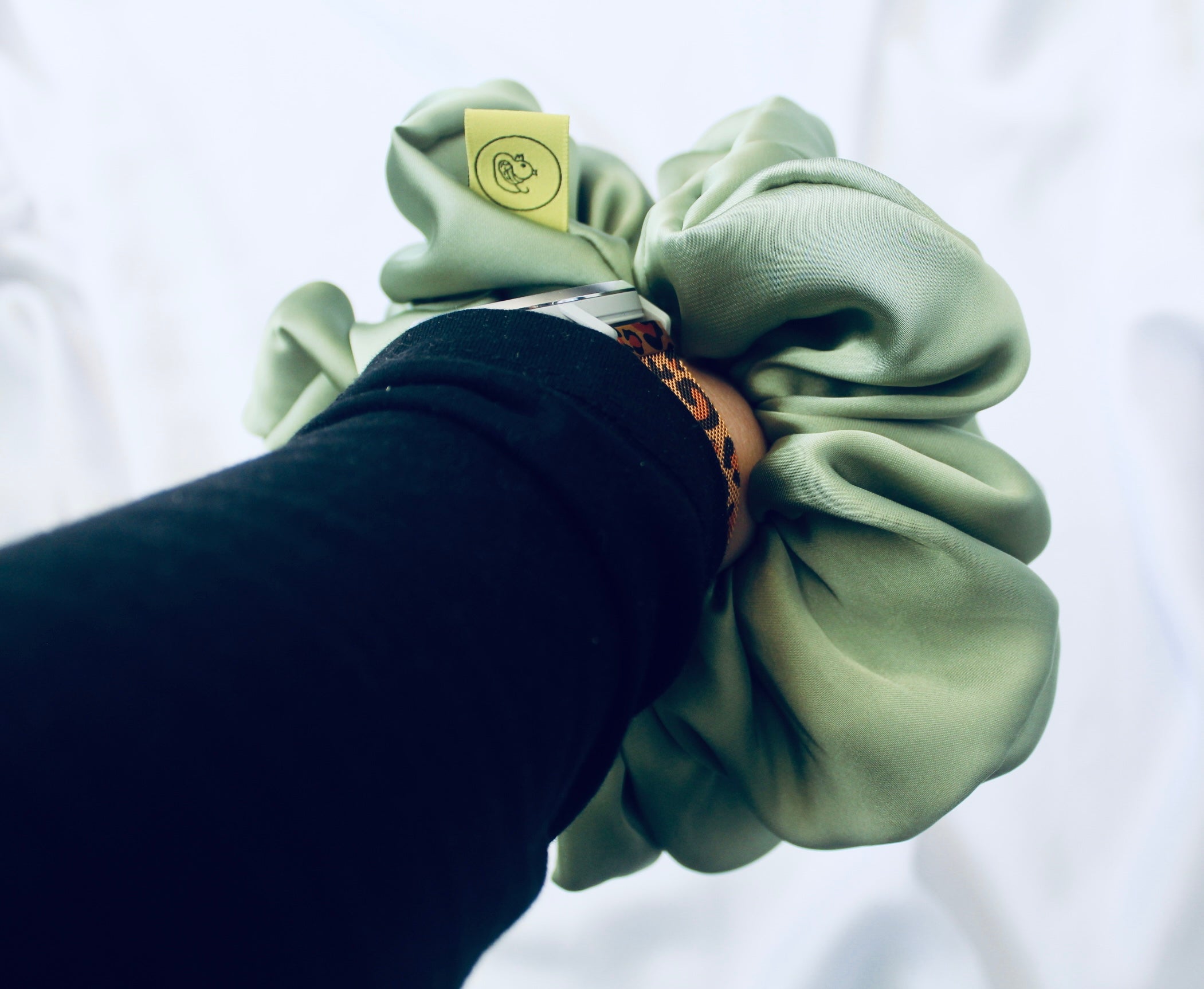 A satin scrunchie in a light green shade with a silky, glossy finish and a ruched design.  Crafted from smooth satin, this scrunchie feels soft and sleek against the hair.  The green tone has a timeless, earthy quality, perfect for both everyday wear and festive styling.  Its ruched fabric is stretched over an elastic band, providing a secure yet comfortable fit.